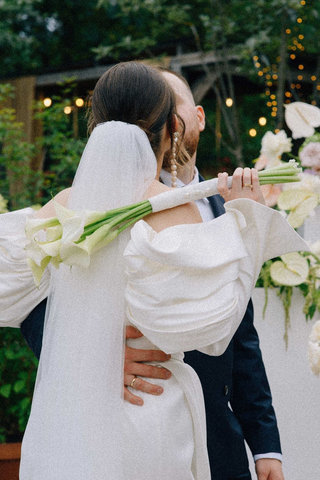 Para Młoda podczas ceremonii ślubnej, panna młoda trzyma bukiet ślubny z białymi kwiatami i zielenią, pan młody w ciemnym garniturze, ogród dekoracyjny w tle.