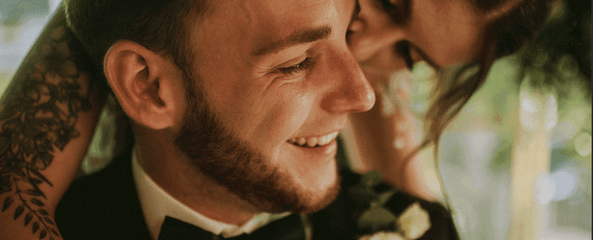 Mężczyzna w garniturze uśmiechający się podczas ceremonii ślubnej, dekoracja kwiatowa bukiet ślubny widoczna w tle