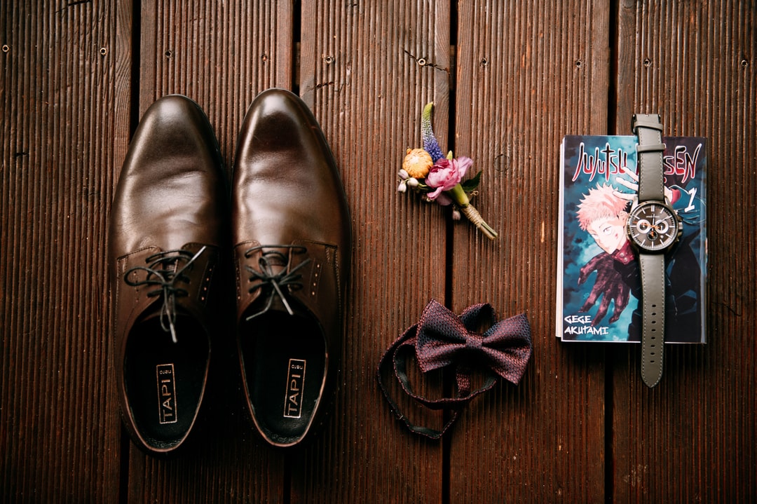 Brązowe skórzane buty, bordowa muszka, kwiaty w pastelowych tonach i zegarek na drewnianym tle