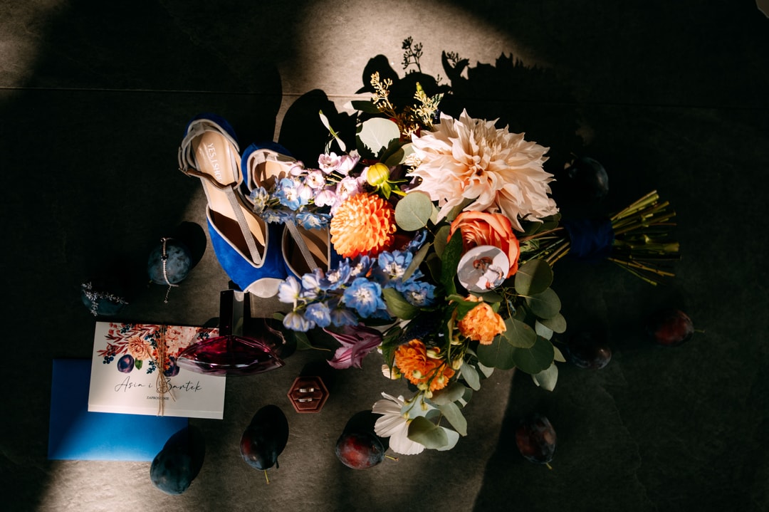 Kompozycja kwiatowa na stół z piwoniami, dalią, różami i błękitnymi kwiatami na ciemnym tle z dodatkami i papeterią.