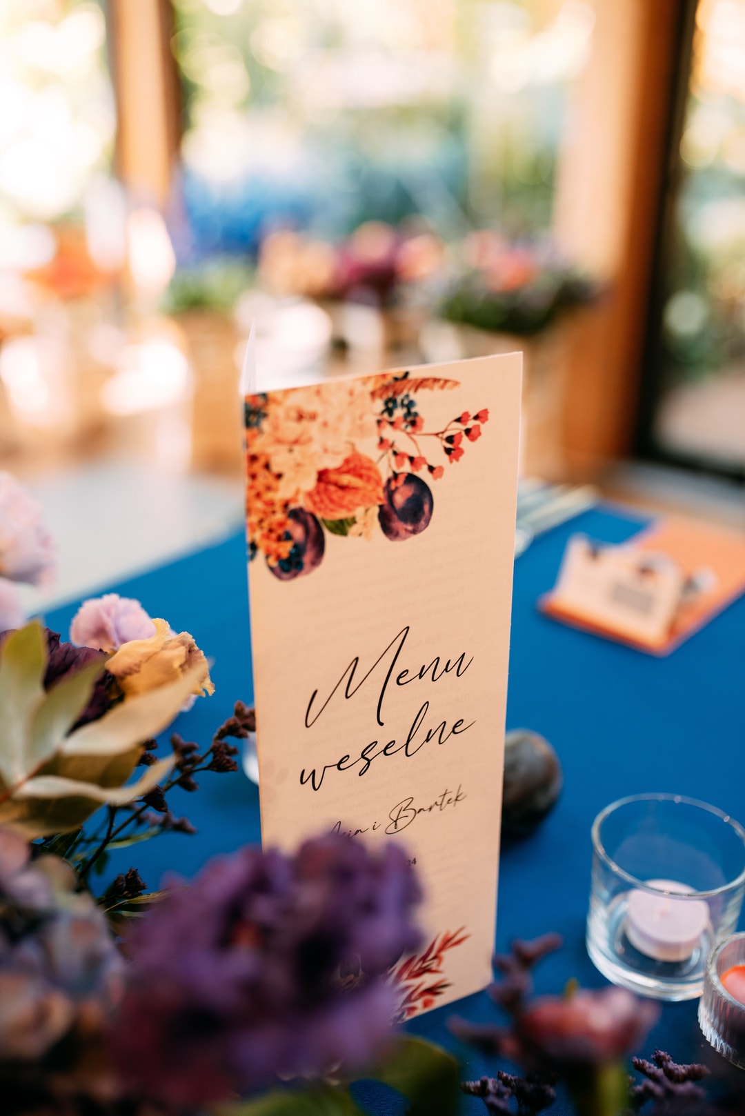 Menu wesselne na niebieskim stole z dekoracją kwiatową, kwiatami i zielenią w tle