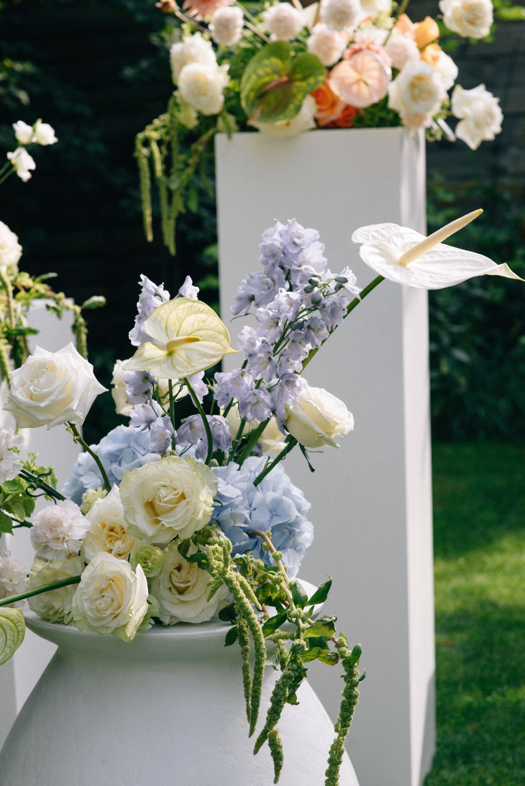 Kompozycja kwiatowa na stół z białymi różami, fioletowymi kwiatami, anturiami i zielenią, w białych wazonach.