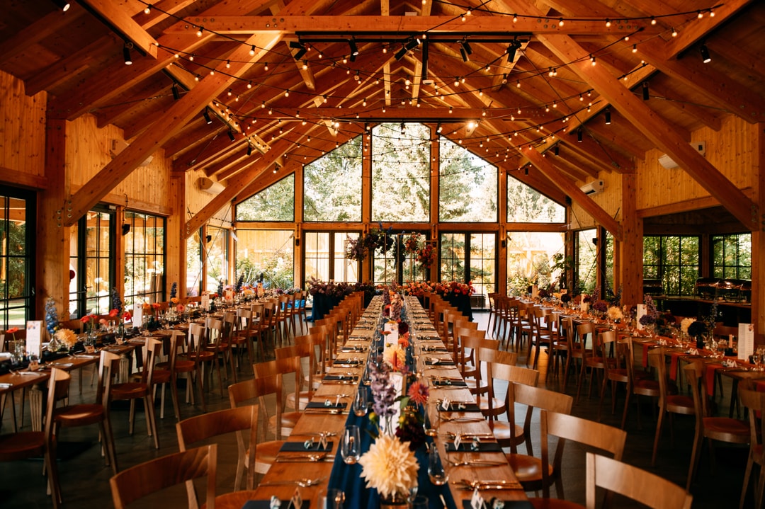 Drewniana sala weselna z dekoracjami sali weselnej, długimi stołami, drewnianymi krzesłami i jasną paletą kwiatów