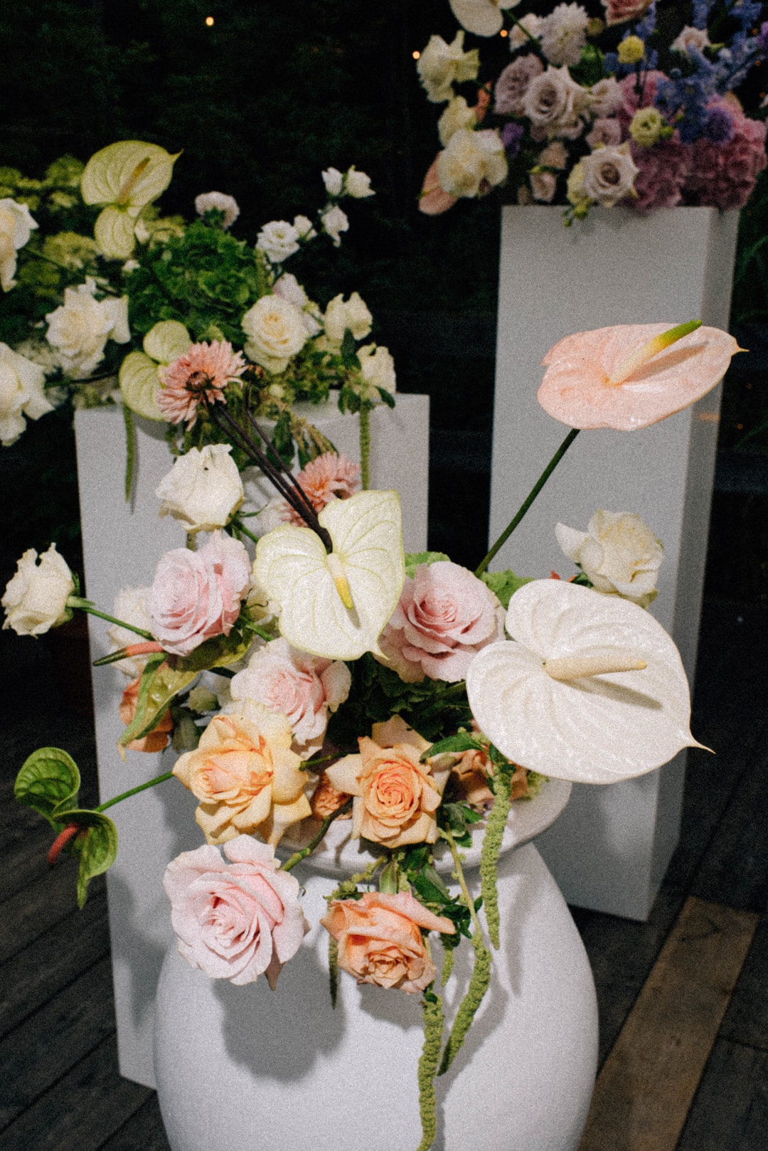 Kompozycja kwiatowa na stół w białych, różowych i pomarańczowych tonach, z anturium, różami i zielenią, w szarym wazonie