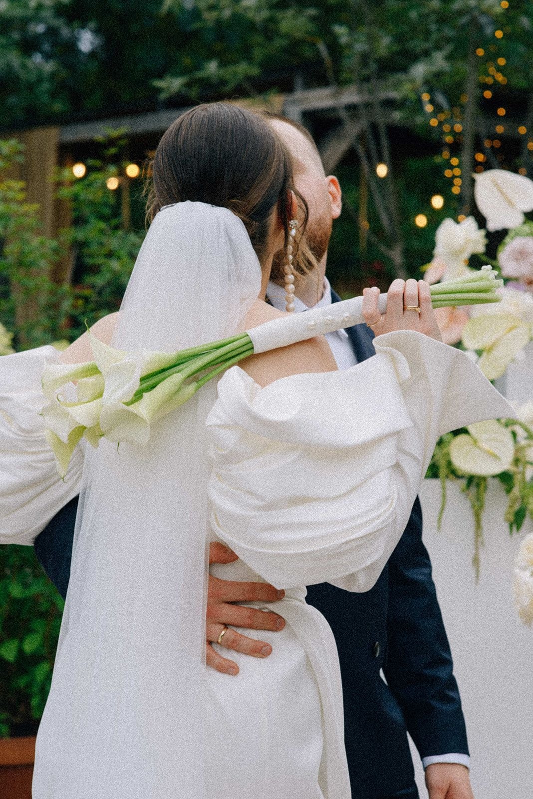 Para Młoda podczas ceremonii ślubnej, panna młoda trzyma bukiet ślubny z białymi kwiatami i zielenią, pan młody w ciemnym garniturze, ogród dekoracyjny w tle.