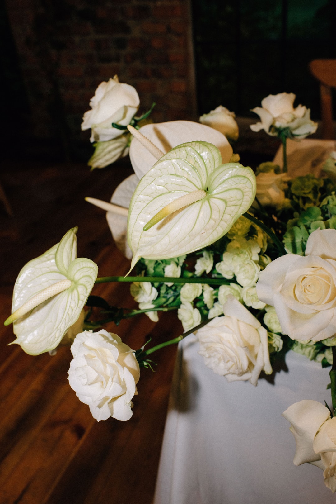 Kompozycja kwiatowa na stół z białymi różami, kwiatami w jasnej palecie i delikatnymi liśćmi na drewnianym tle