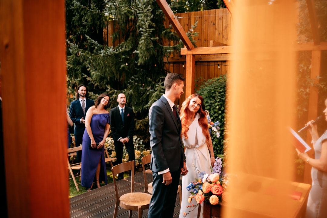 Para Młoda podczas ceremonii ślubnej w ogrodzie, dekoracje sali weselnej z kwiatami w jasnej palecie, goście w tle