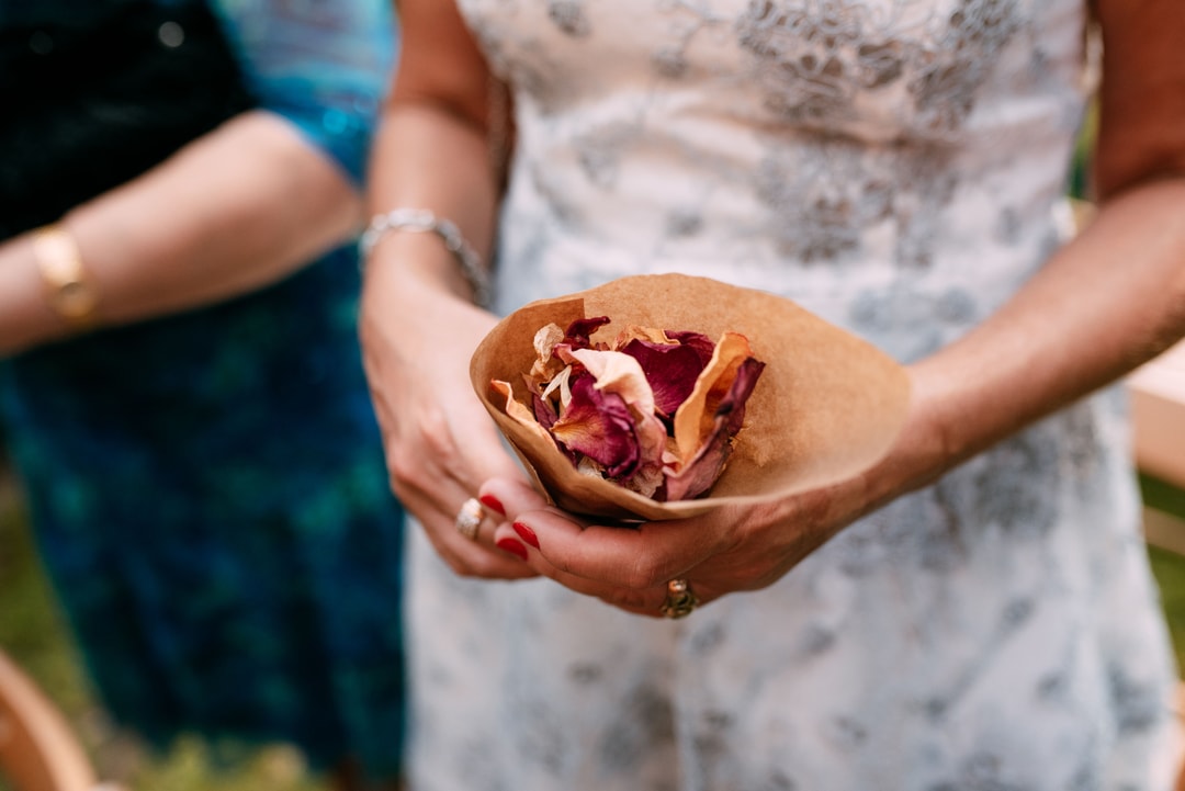 Dwie osoby trzymają papierowy stożek z suszonych kwiatów w odcieniach bordo i pomarańczu, kompozycja kwiatowa na stół w naturalnych tonach.