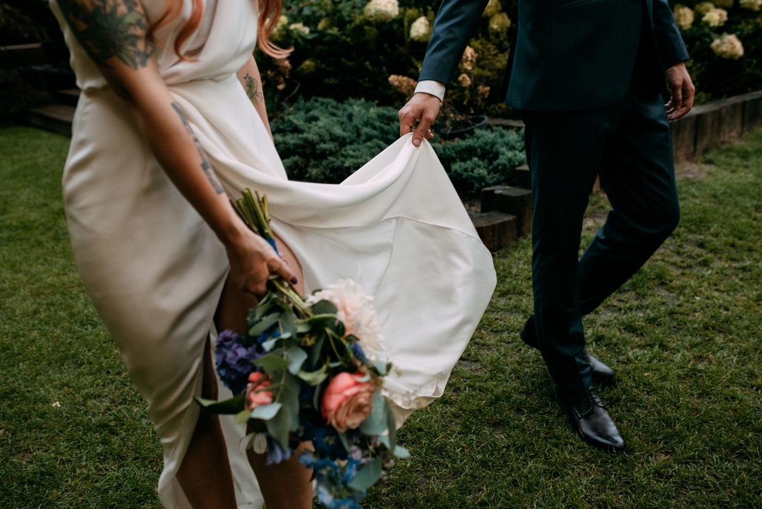 Para Młoda trzymająca bukiet ślubny z kwiatami w ciepłych tonach, na tle zieleni ogrodowej