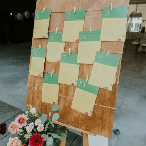 Drewniana tablica z numerowanymi karteczkami i kwiatami jako dekoracja na imprezę. Naturalne tło z drewna.