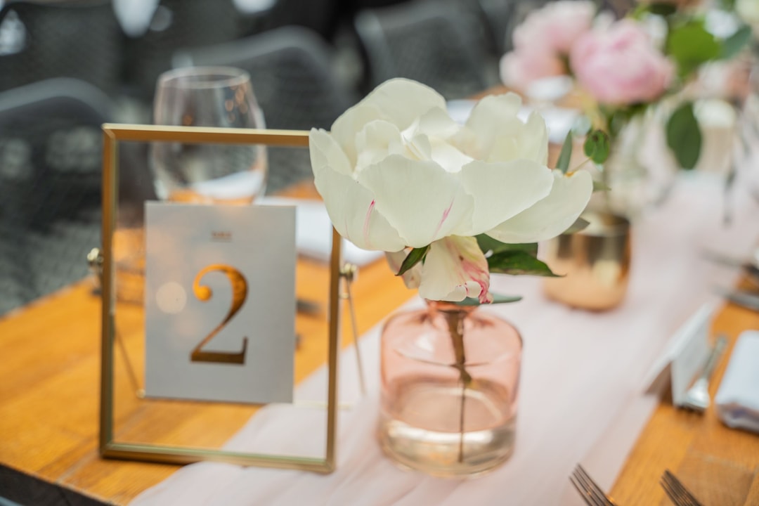 Dekoracja stołu weselnego z numerem 2, białymi kwiatami w różowym wazonie