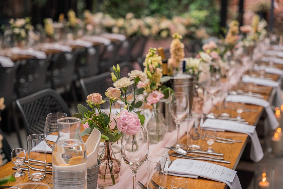 Elegancki wystrój sali weselnej z drewnianymi stołami, różowymi kwiatami i delikatnymi świecami