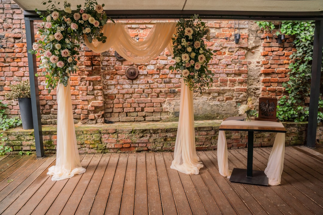 Rustykalna dekoracja ślubna z kwiatami i draperią na tle starej ceglanej ściany