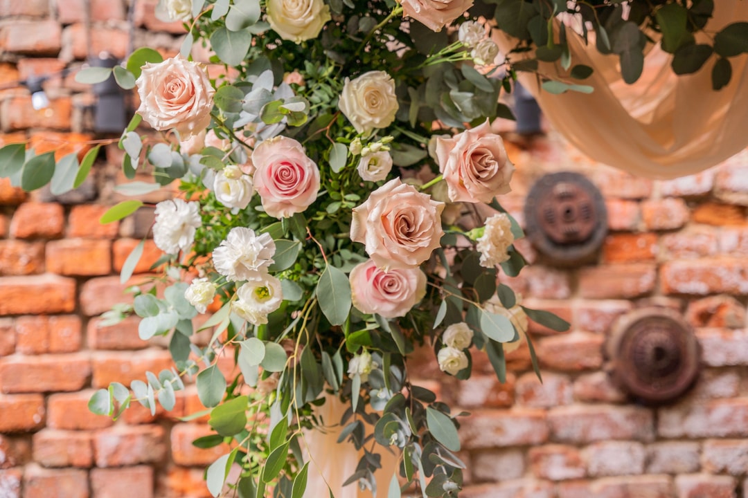 Bukiet ślubny z różowych róż, białych kwiatów i zielonych liści na ceglastym tle