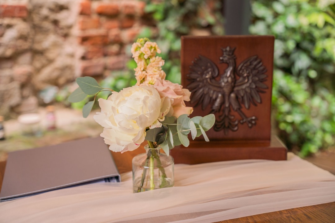 Kwiatowa kompozycja ślubna z białymi piwoniami obok herbu Polski