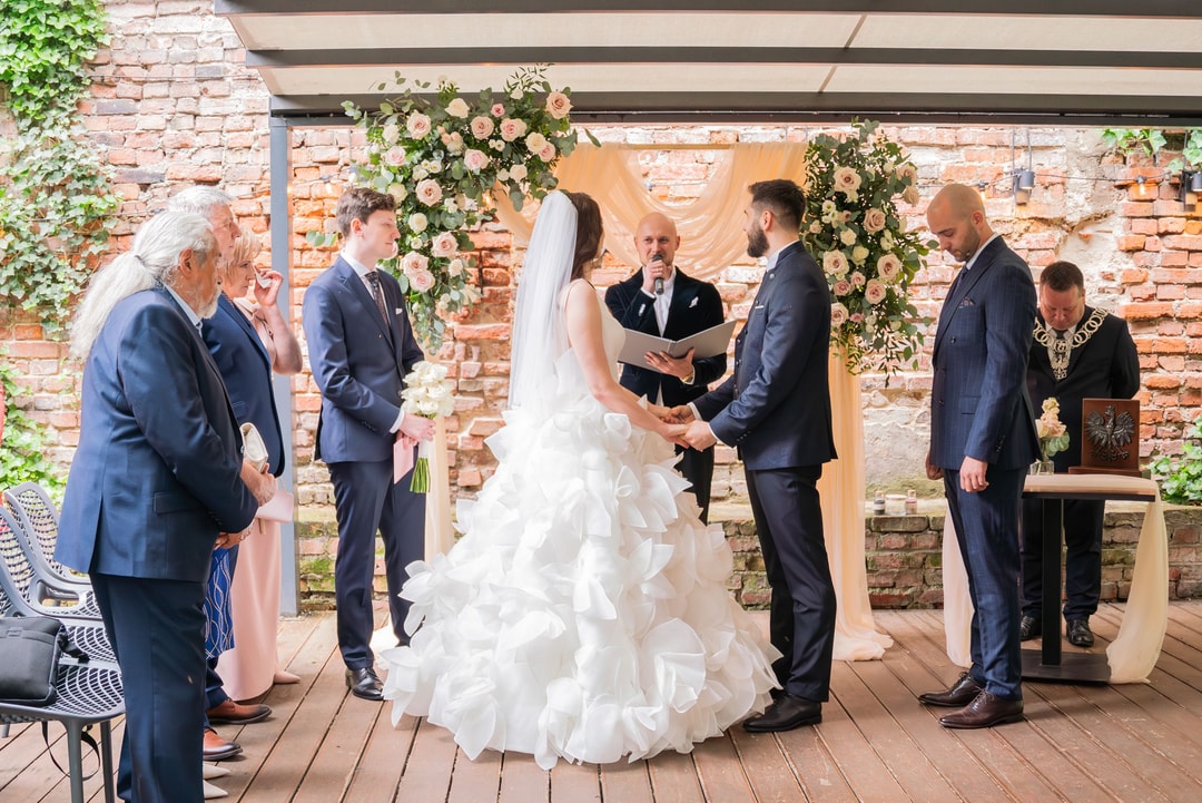 Ceremonia ślubna z kwiatową dekoracją łuku i zabytkową ścianą z cegły
