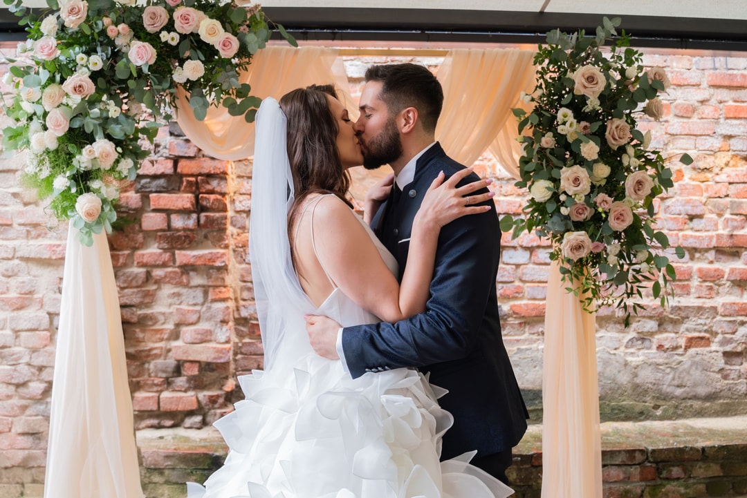 Para młoda całująca się pod kwiatowym łukiem z różami