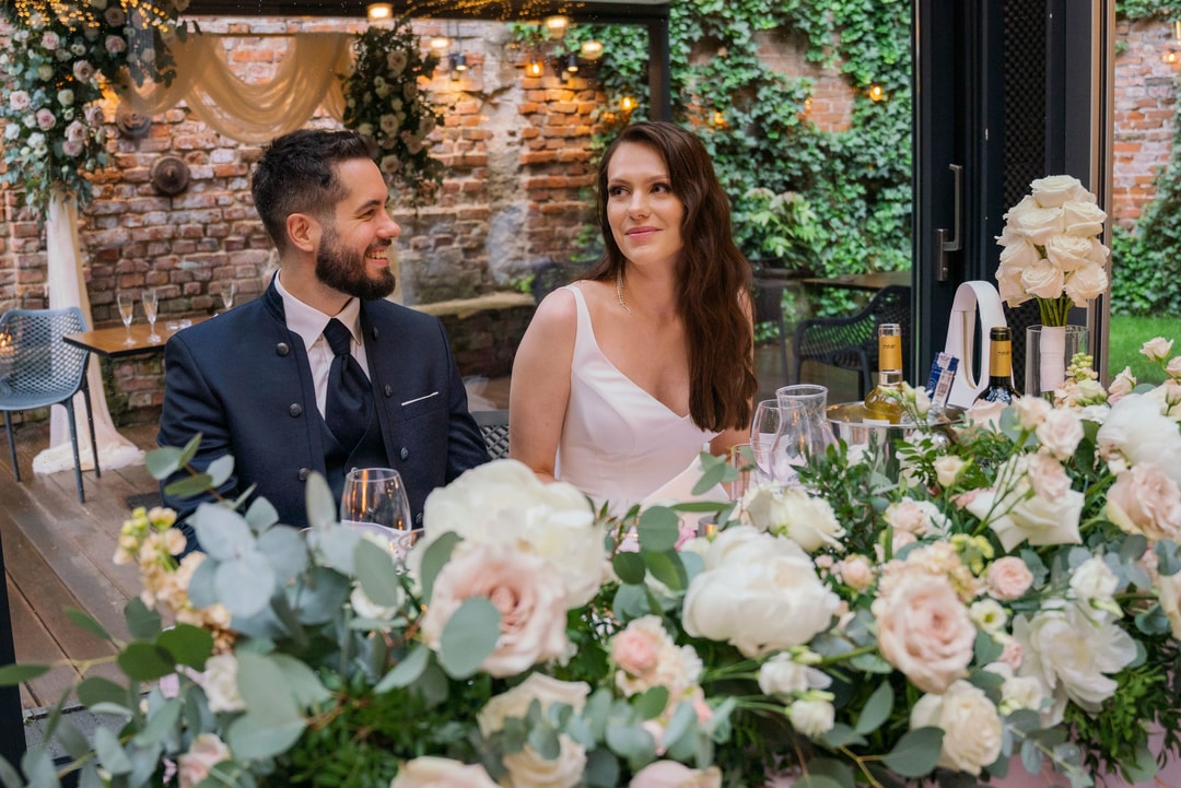 Elegancka para młoda przy stole weselnym, otoczona białymi i różowymi różami w rustykalnym wnętrzu