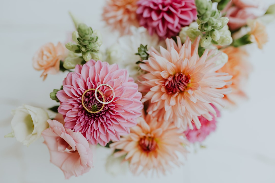 Złote obrączki ślubne na różowej dahlli i brzoskwiniowych kwiatach w kompozycji kwiatowej na stół