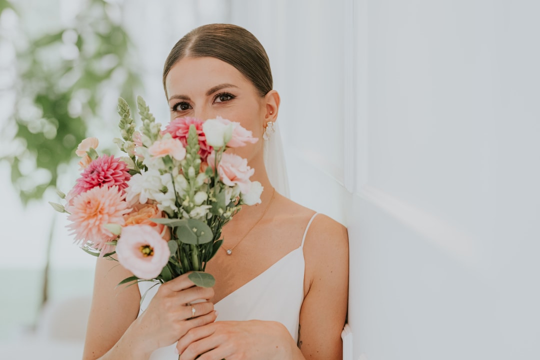 Kobieta trzymająca букiet ślubny z różowymi i białymi kwiatami, zieleń, jasne tło, delikatna aranżacja kwiatowa.