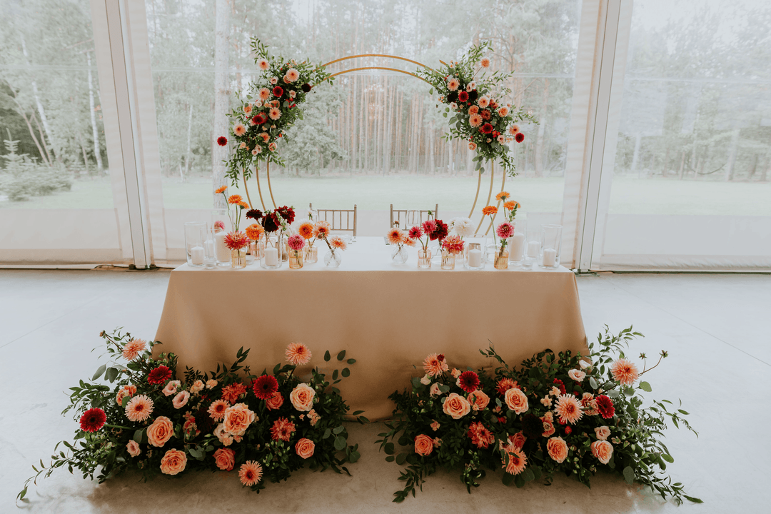 Dekoracje sali weselnej z łukiem kwiatowym w tonach pomarańczowym i czerwonym, stół prezydialny, duża witryna.