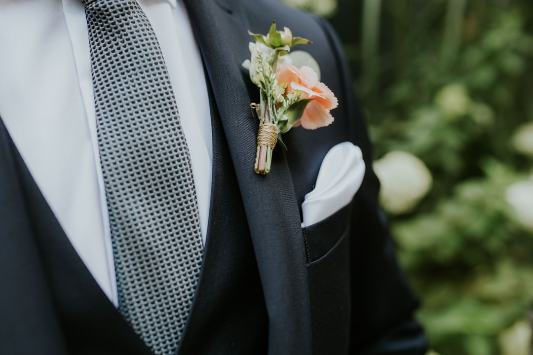 Butonierka ślubna z delikatnymi kwiatami w pastelowych tonach, zawiązana sznurkiem, przypięta do marynarki pana młodego