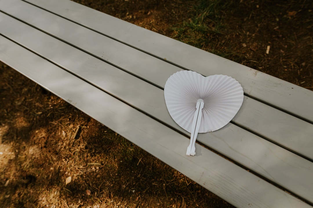 Biały papierowy wentylator w kształcie serca na białym drewnianym podłużnym stole, ziemia w tle