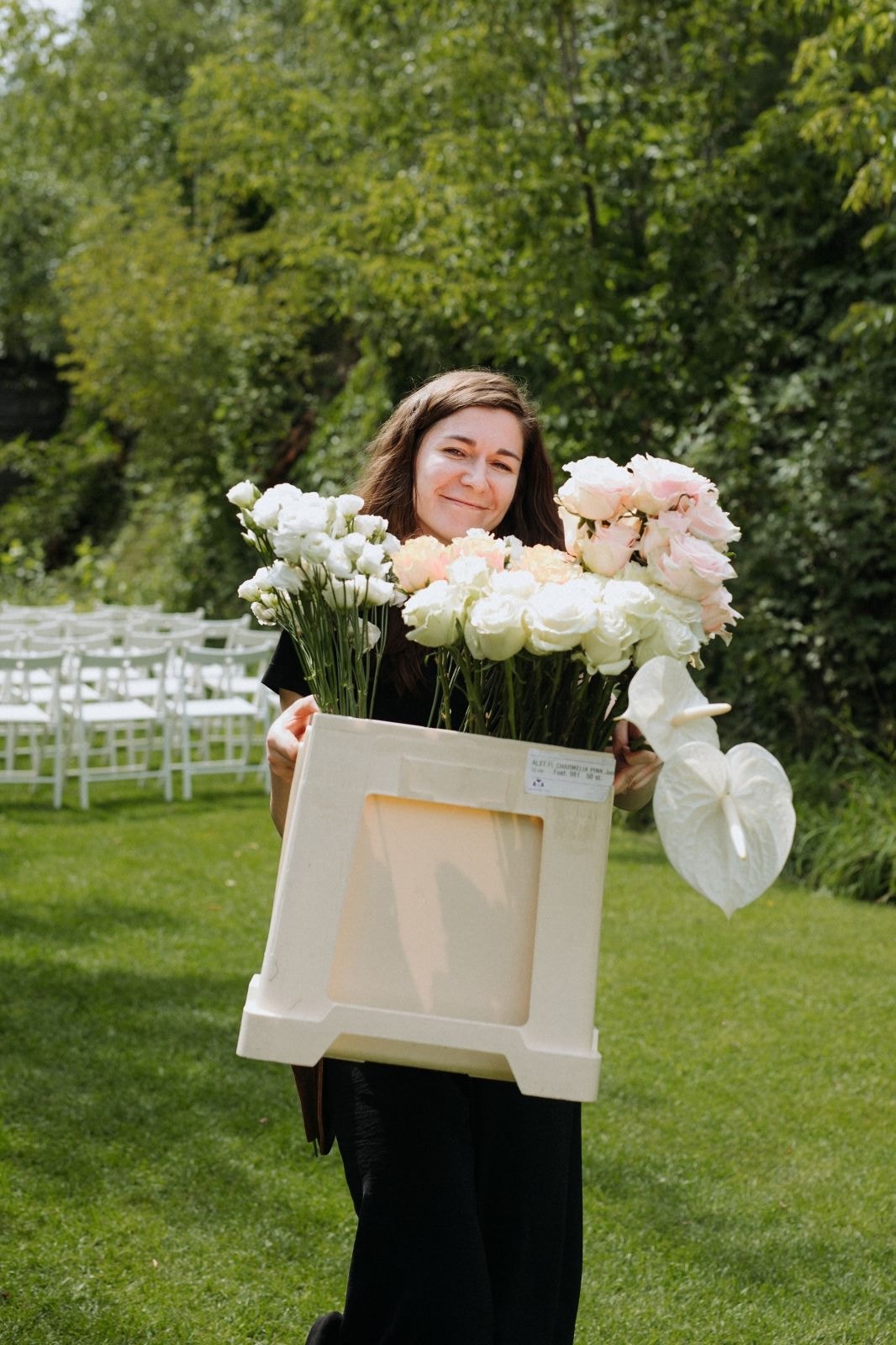 Florystka przenosząca kwiaty na tle przygotowań do ślubu w plenerze