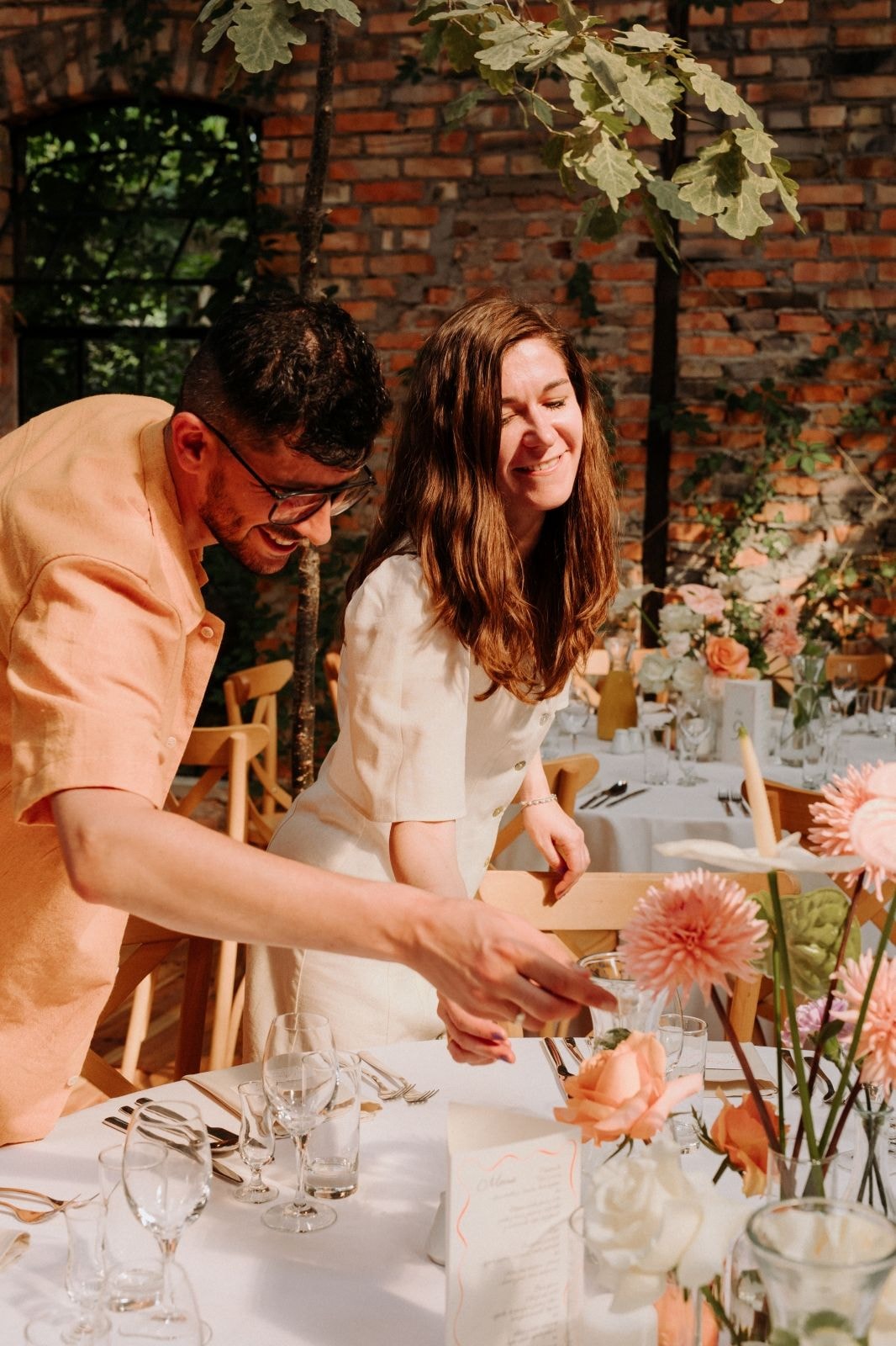aranżacja stołu weselnego z różowymi daliami i pomarańczowymi różami, para w otoczeniu ceglanej ściany i liści