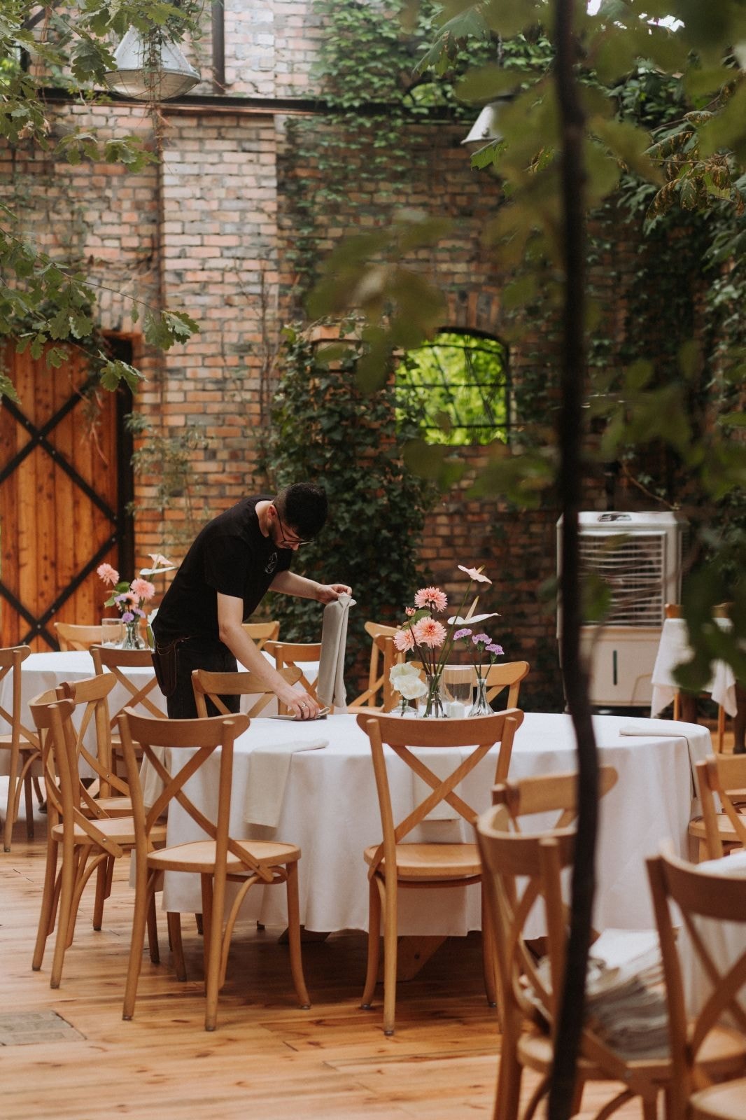 Rustykalne wesele: eleganckie stoły z różowymi daliami, białymi obrusami i drewnianymi krzesłami w ceglanych wnętrzach