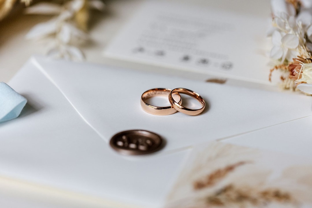 Dwie złote obrączki ślubne na białej papeterii z wysuszonymi kwiatami i pieczęcią