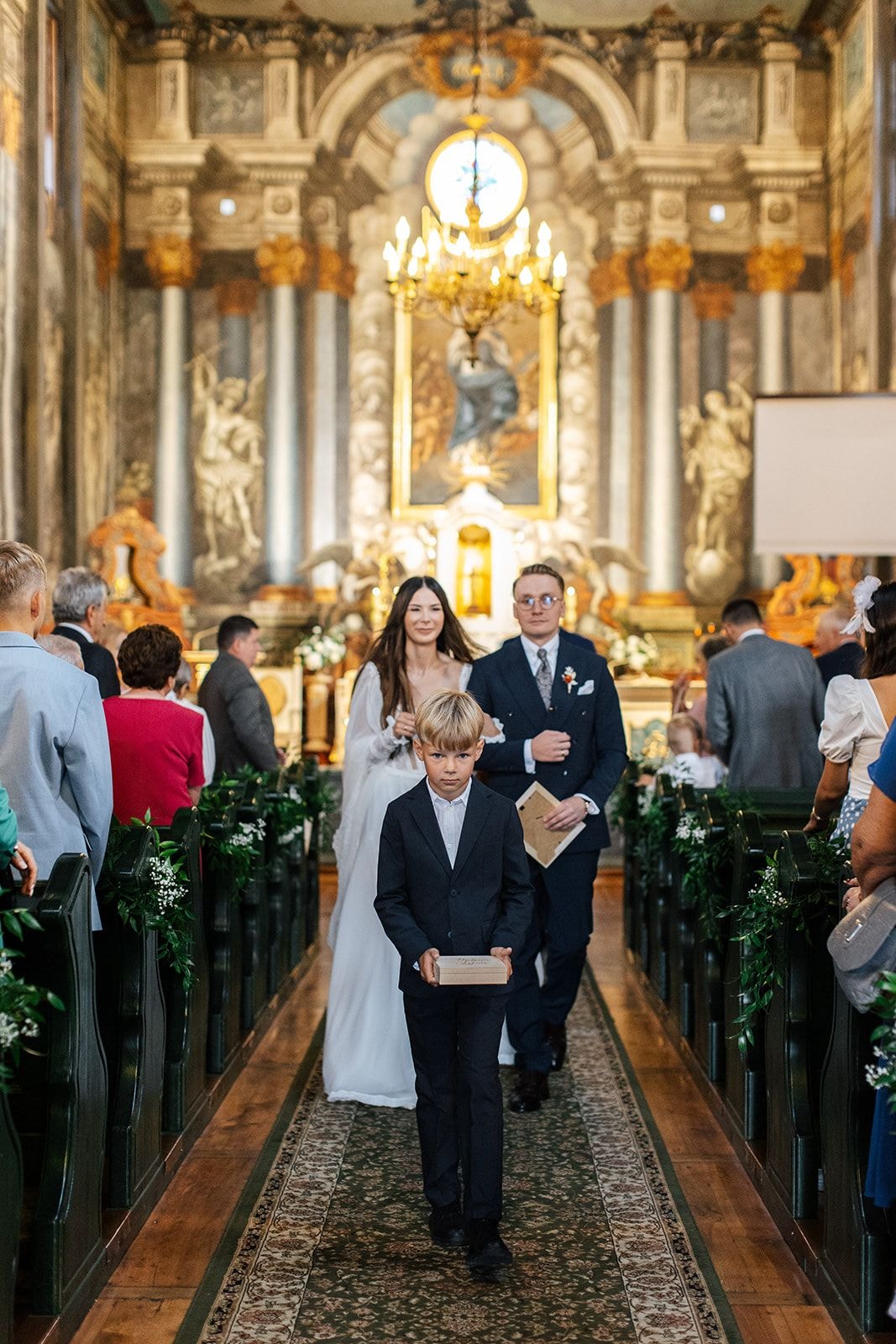 Dekoracje sali weselnej: alejka z zielenią, parasol słoneczny, żyrandol, ołtarz i państwo młodzi z dzieckiem