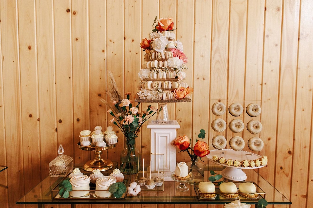 Wysoka kompozycja na stół z makronami w jasnej palecie, białymi i łososiowymi kwiatami, na drewnianym tle sali