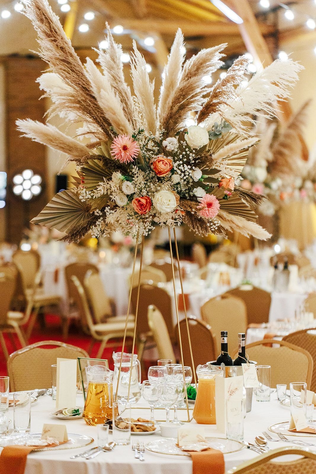 Dekoracja stołu weselnego z kompozycją kwiatową na wysoki stojak, kwiaty w tonach łososiowych, białych i pastelowych z pampasami.