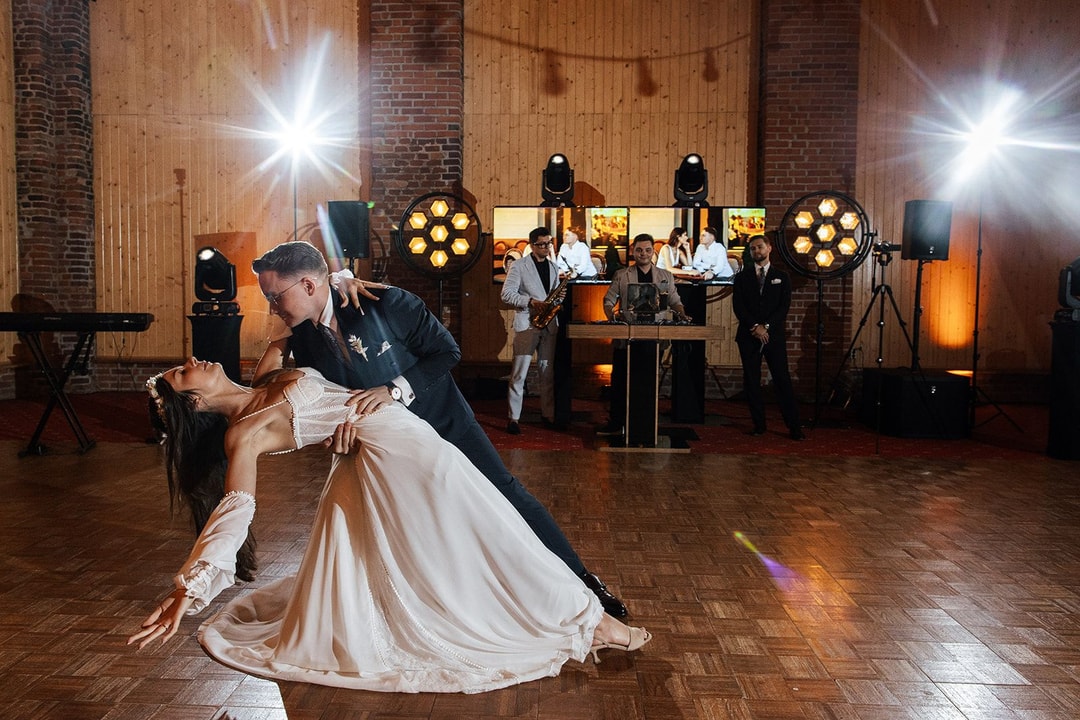 Para młoda podczas pierwszego tańca na parkiecie w drewnianej sali weselnej, z oświetleniem scenicznym i gośćmi w tle