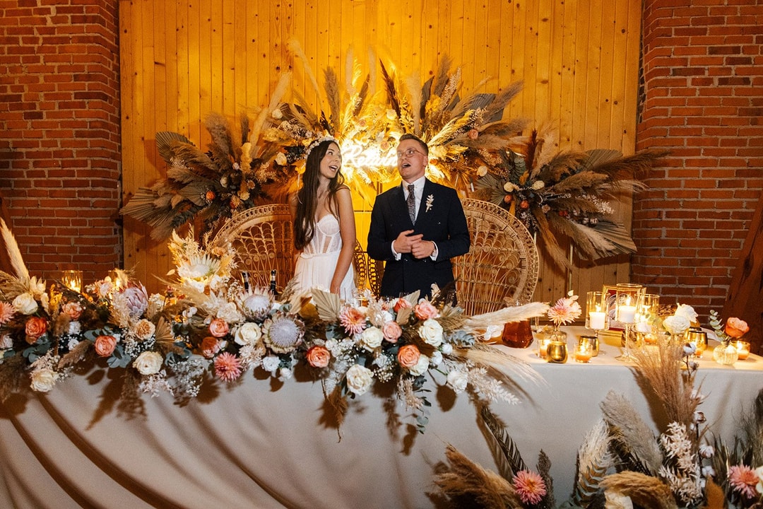 Dekoracja stołu prezydialnego z kompozycją kwiatową w pastelowych tonach, suchymi trawami, świecami i drewnianym tłem