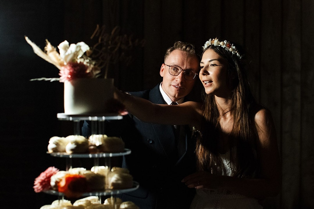 Trójpiętrowy tort weselny z białymi i różowymi kwiatami, para młoda admira ujące dekorację tortu przy czarnym tle.