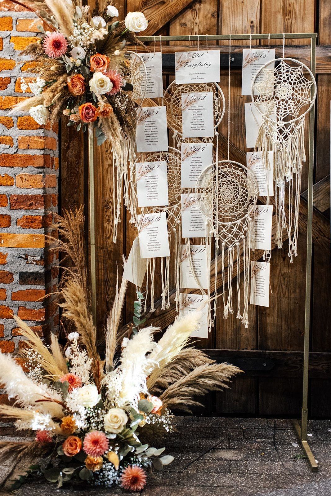 Tablica seatingowa z motywem łapacza snów - papeteria ślubna zawieszona na metalowej ramie z dekoracjami kwiatowymi