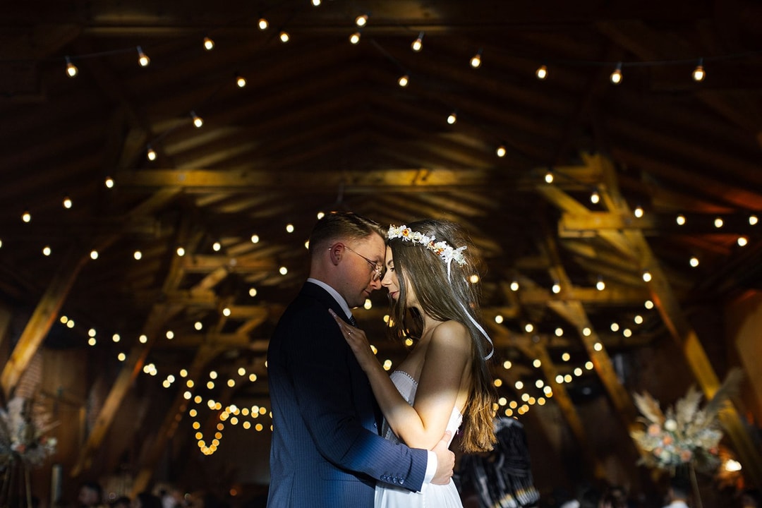 Para Młoda w obejmie pod dekoracją sali weselnej z żółtymi światłami i drewnianymi belkami