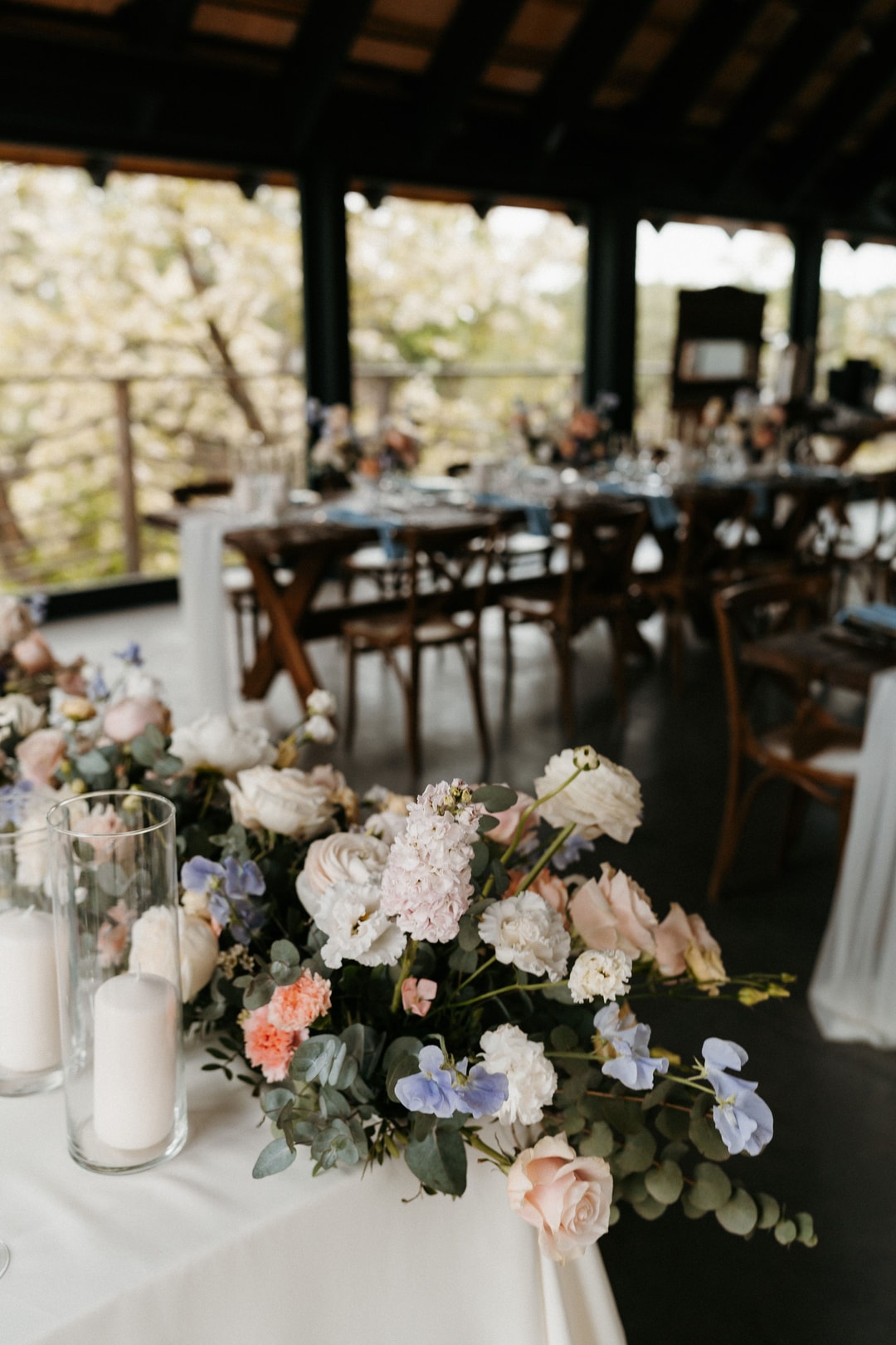 Kompozycja kwiatowa na stół z białymi i różowymi kwiatami, delikatną zielenią oraz świeczką, pod zadaszeniem sali weselnej