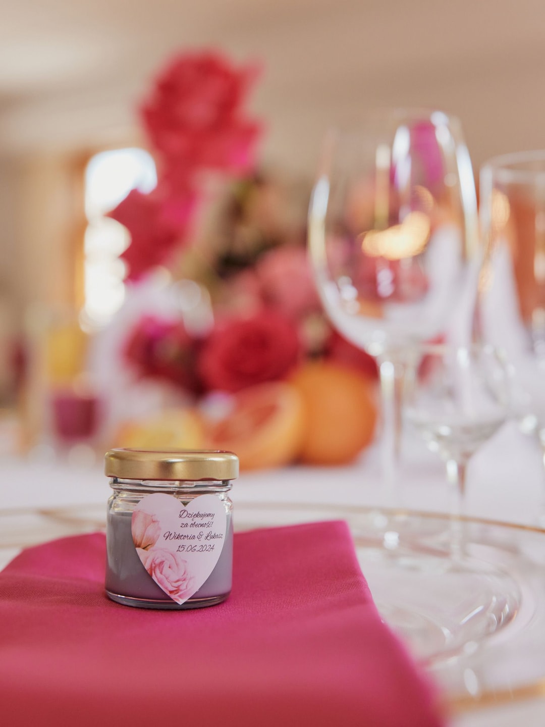 Słoiczek z dekoracją kwiatową na różowym obrusie, aranżacja stołu weselnego z kieliszkami i kwiatami w tle