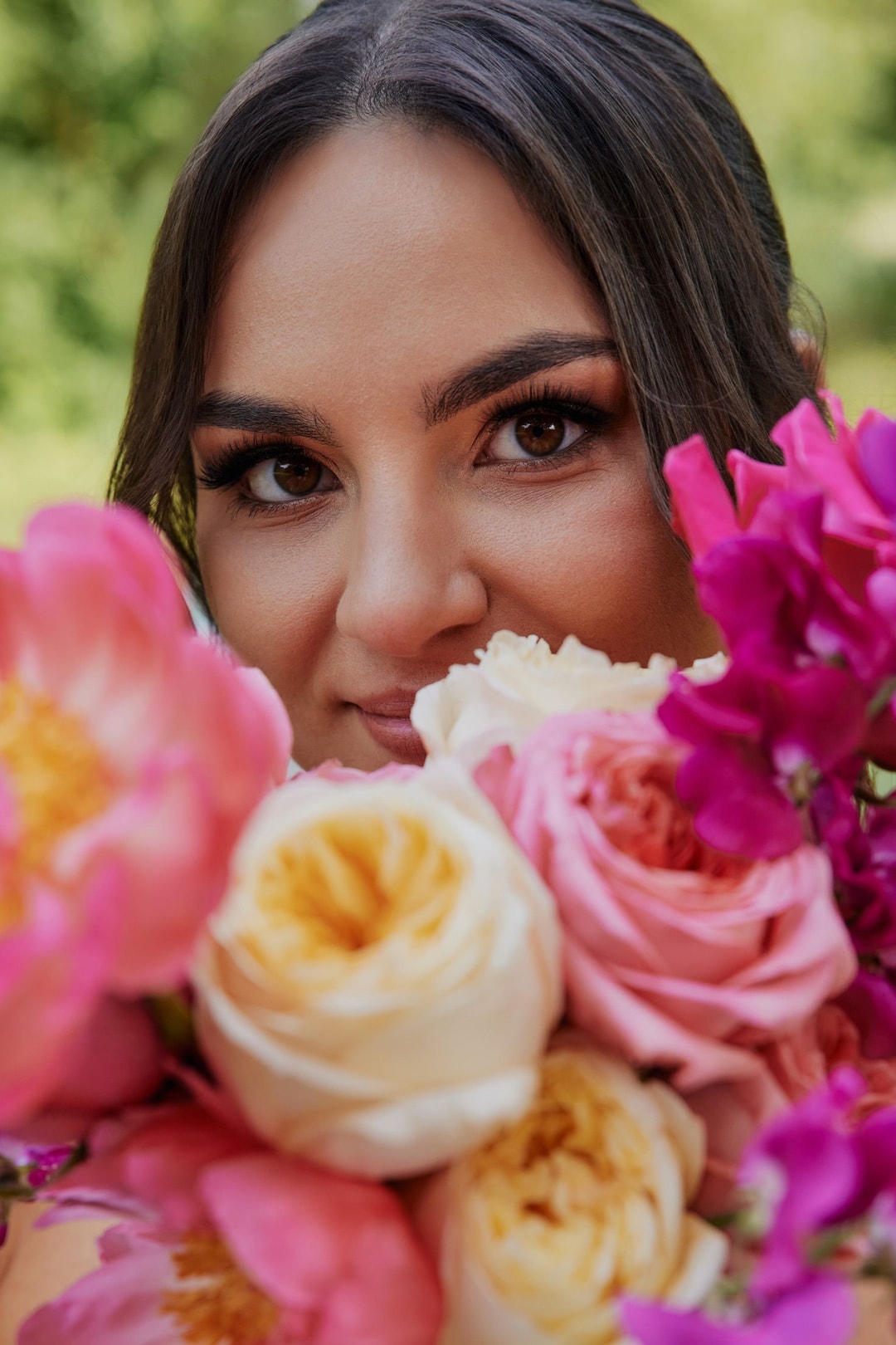 Kobieta przy kompozycji kwiatowej z różami w tonacji jasnej i różu, otoczona zielenią