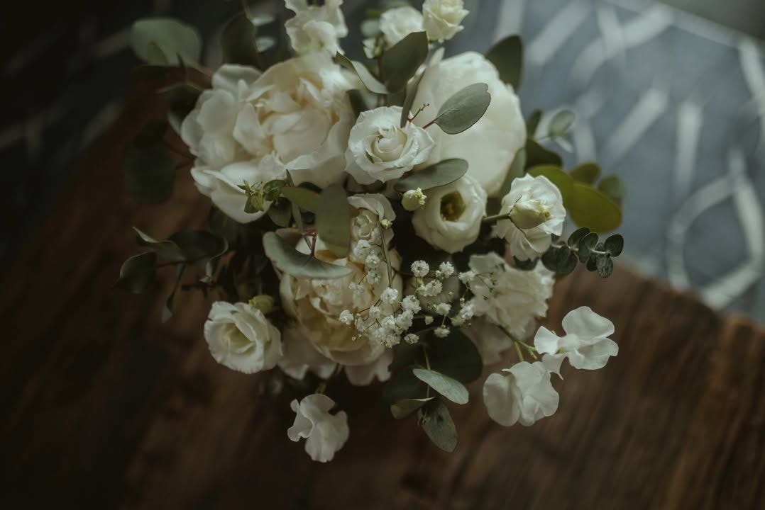 Delikatna kompozycja kwiatowa na stół z białymi różami, małymi kwiatkami i zielenią eukaliptusa na drewnianym tle