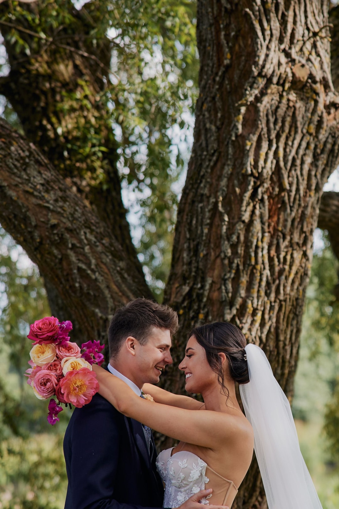 Para Młoda trzymająca bukiet ślubny z różowymi i pełnymi peonami pod starym drzewem pokrytym mchem