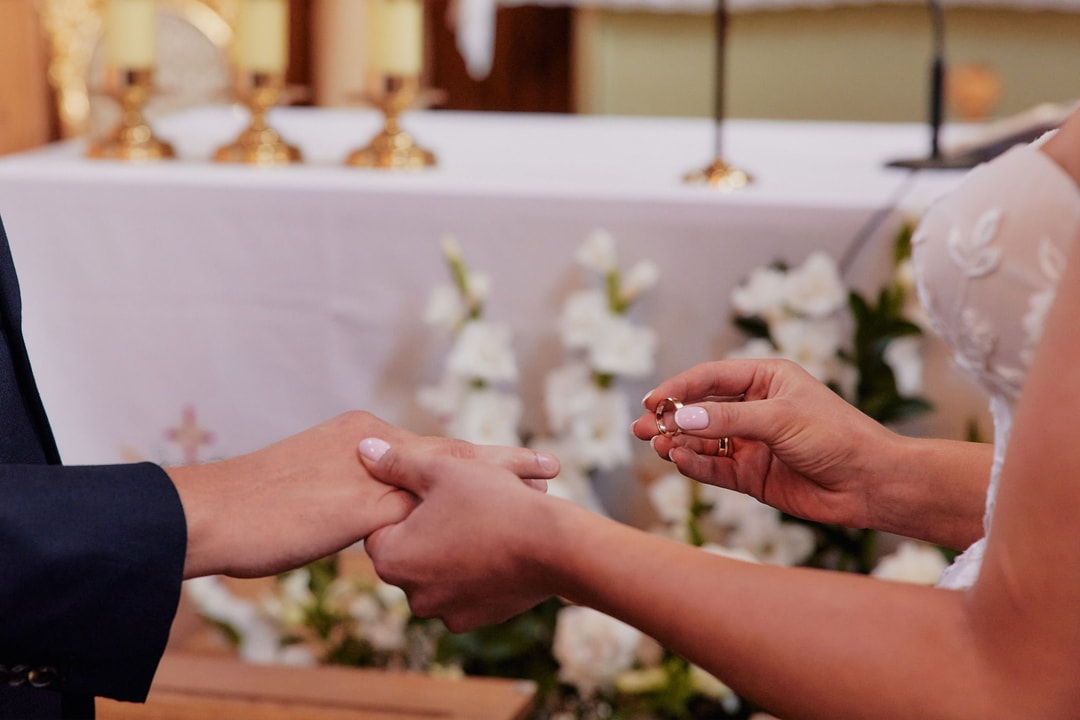 Para Młoda wymieniająca obrączki ślubne, w tle dekoracja stołu z białymi kwiatami