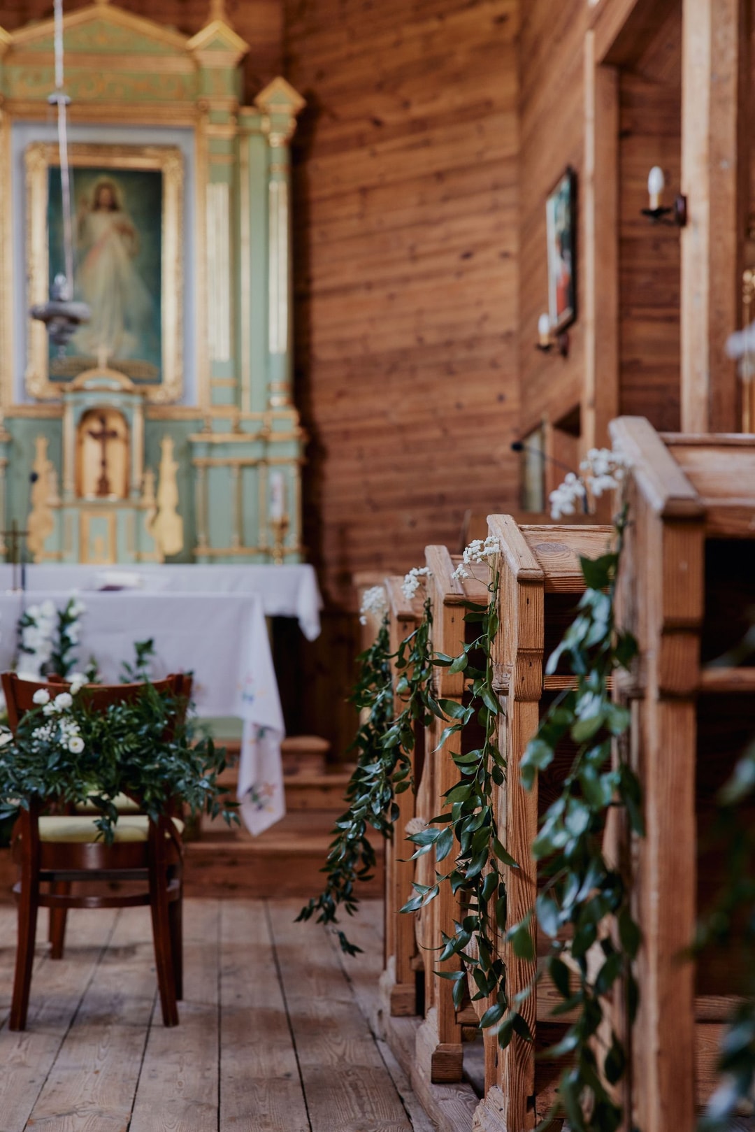 Drewniana kaplica z zielenią oplatającą ławki, dekoracje sali weselnej, ołtarz z obrazem i białym obrusem