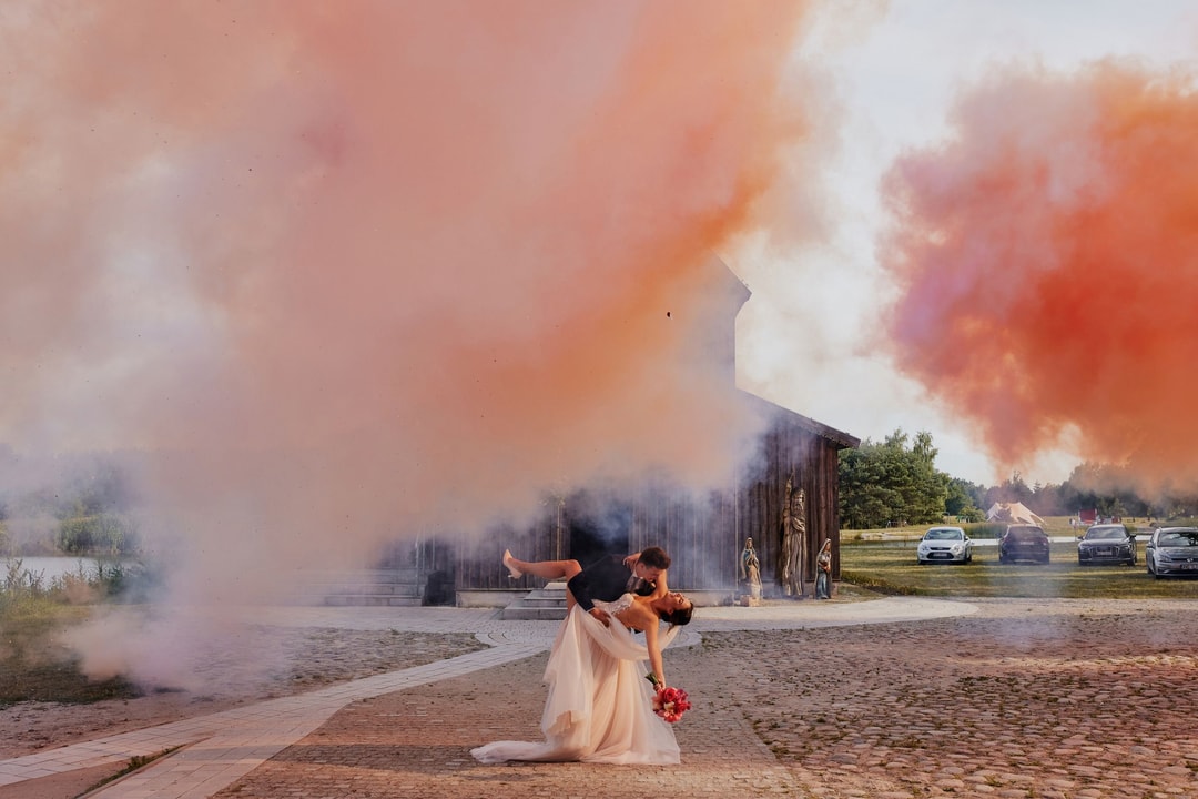 Para w strojach ślubnych podczas ceremonii na plaży z kolorowym dymem, dekoracje sali weselnej w tle