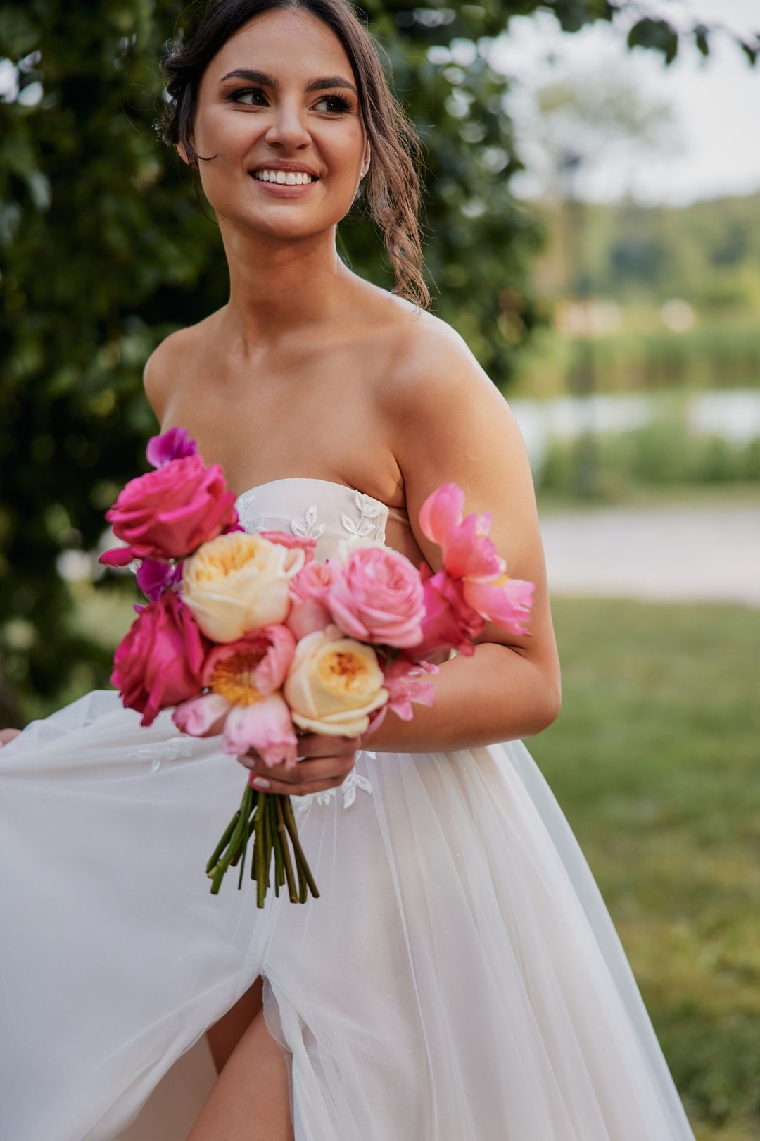 Kobieta w białej sukni trzymająca bukiet ślubny z różowymi i żółtymi różami na tle ogrodu