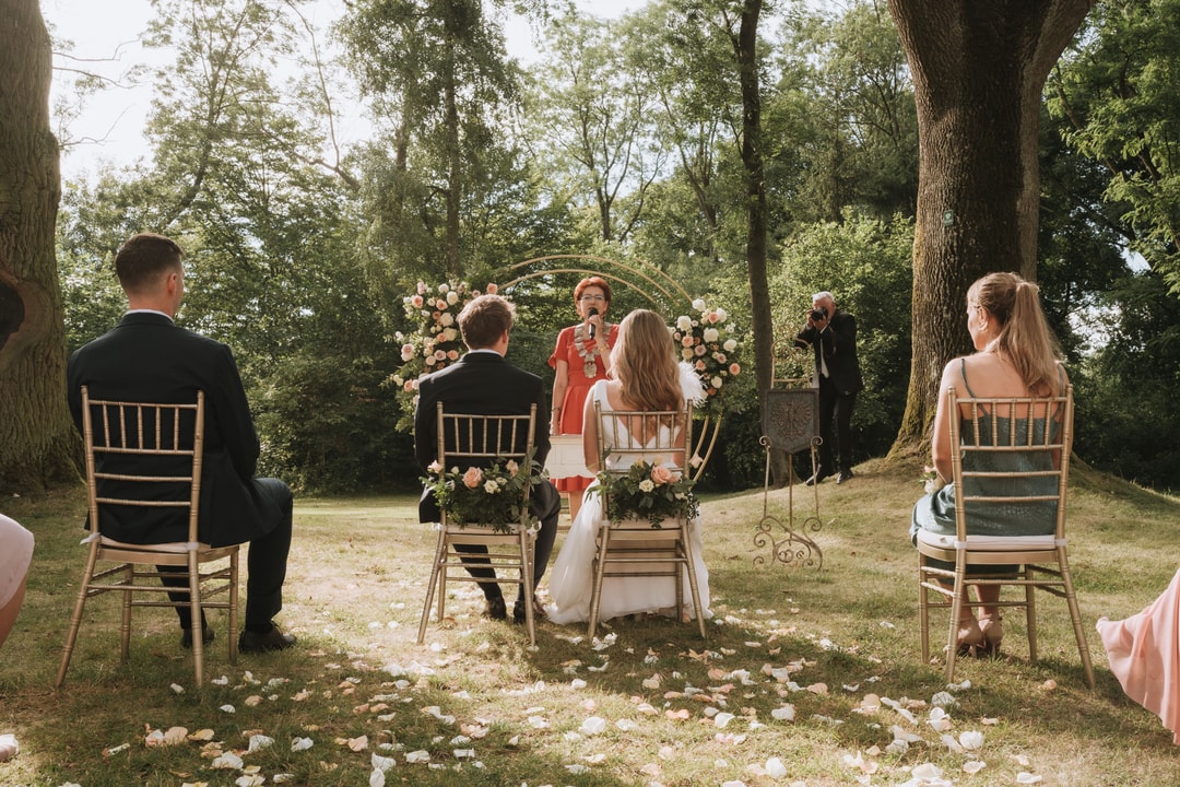Łuk kwiatowy z różowymi i białymi kwiatami, panna młoda w białej sukni i pan młody w czarnym garniturze podczas ceremonii ślubnej w ogrodzie.