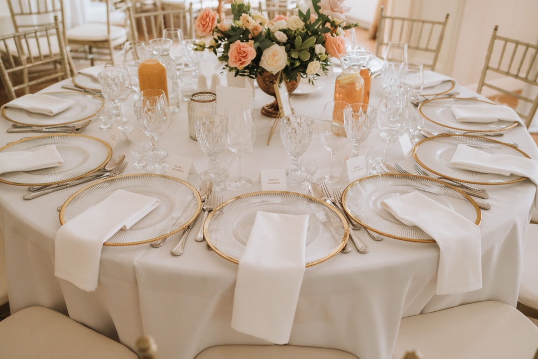 Aranżacja stołu weselnego z białym obrusem, złotymi talerzami i naturalnymi kwiatami w pastelowych tonach